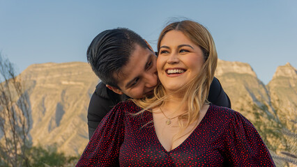 young hispanic man kisses his partner on the back of her neck as she smiles