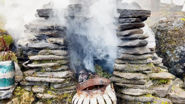Holy puja ceremony fireplace. Smoke flying up and covering Holy buddhist praying multicolored flags with mantras slow motion video in Tuli Kharka village at 4200m on Mera peak climbing route.