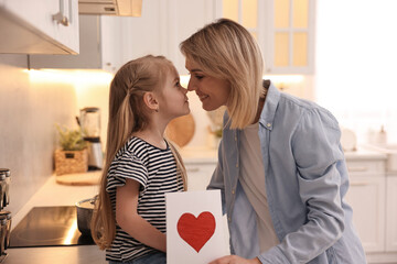Little daughter congratulating her mom with greeting card in kitchen. Happy Mother's Day
