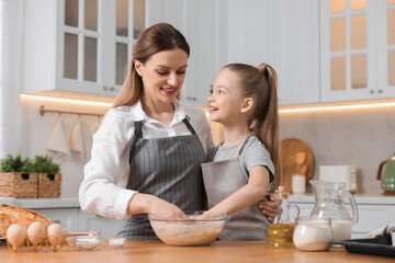 Making bread. Mother and her daughter kneading dough at wooden table in kitchen