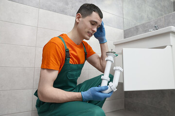 Thoughtful plumber wearing protective gloves repairing sink in bathroom