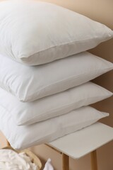 Stack of soft white pillows on table near beige wall