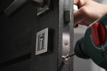 Naklejka premium Handyman with electric screwdriver repairing door handle indoors, closeup