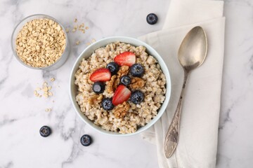 Tasty oatmeal with strawberries, blueberries and walnuts served on white marble table, flat lay