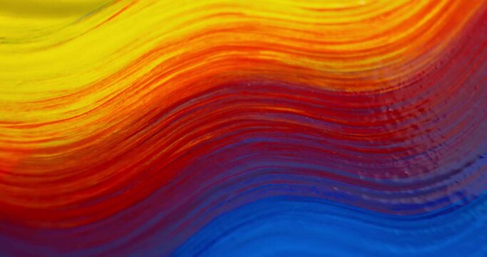 Close up of an artist's paintbrush with brush stroke painting primary colors of red, blue, and yellow paint lines across the canvas creating a rainbow of vibrant colors background.