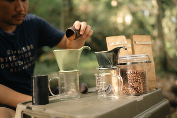 A man is pouring coffee into a cup from a gold pot. The scene is set in a natural environment, with...