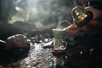 A man is pouring coffee into a cup from a gold pot. The scene is set in a natural environment, with...