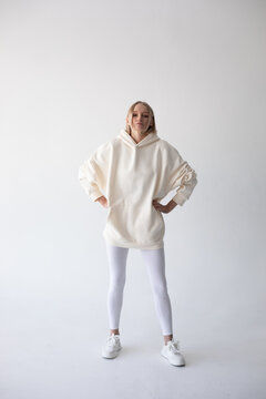 Blonde girl in a white hoodie and tights posing on a white background