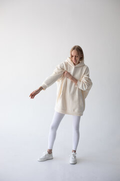 Blonde girl in a white hoodie and tights posing on a white background
