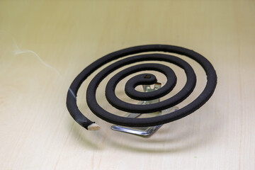 Burning mosquito repellent coil on a wooden background. The coil's active ingredient evaporates...