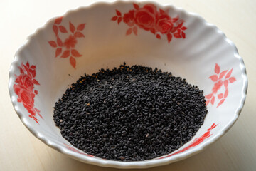 Black cumin seeds heap on a white melamine bowl on a wooden background. Locally in Bangladesh, it is called Kalojira and its scientific name is Nigella sativa. 