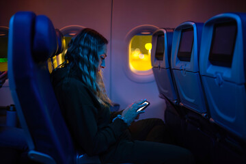 Woman passenger sitting in her seat on an airplane and browsing the internet on her mobile phone...