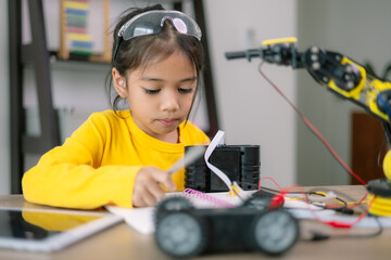 A young girl is sitting at a desk with a robot toy in front of her