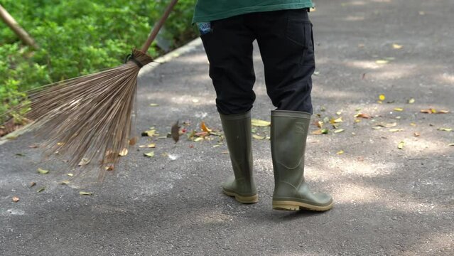 Gardener sweeping using broom stick on a sidewalk of park. Slow motion, 4k resolution.
