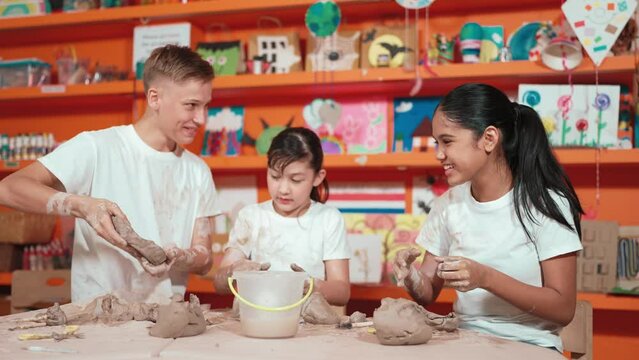 Multicultural happy student playing by throw clay while modeling cup in pottery class. Caucasian high school girl pointing at boy while smiling smart boy laughing at art lesson. Education. Edification