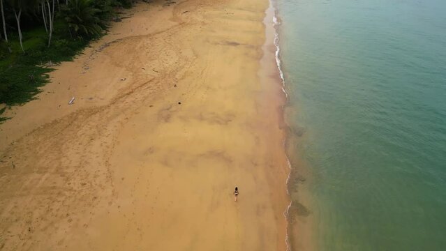 Aerial tilt shot of a person walking across a empty beach in cloudy Sao Tome