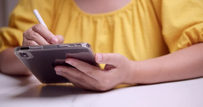 Browsing the internet, the woman is using her tablet and a stylus pen to check her messages and update her social Media status using the internet.