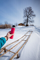 Pink thermos on tree background, winter trekking in the forest, hand holding thermos with hot drink, walk in spring park.