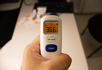 Latin man's hand holding an infrared thermometer indicating normal body temperature.