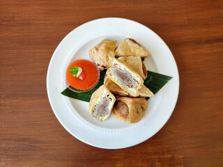 Delicious fried meatball tofu or tahu bakso goreng or fried tuna tofu or tahu tuna goreng as a healthy snack with spicy chili sauce on a white plate on a brown wooden table