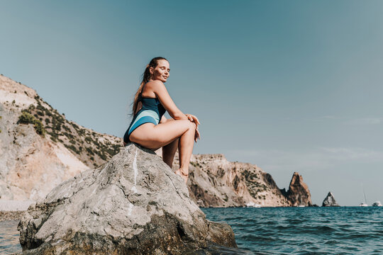 Woman beach vacation photo. A happy tourist in a blue bikini enjoying the scenic view of the sea and volcanic mountains while taking pictures to capture the memories of her travel adventure.
