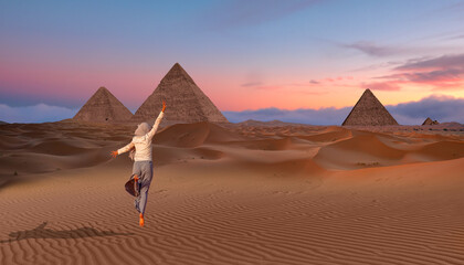 Muslim woman in gray trousers and a scarf jumps on the sands of the Sahara desert -  Giza Pyramid...