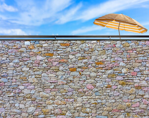 Parasol de plage derrière mur de pierres - obrazy, fototapety, plakaty