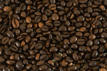 Naklejka premium Close-up of freshly roasted coffee beans piled on a wooden table, creating a rich and aromatic background.