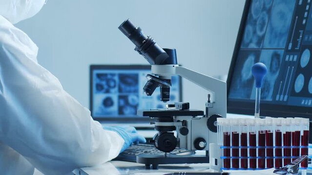 Scientist in protection suit and masks working in research lab using laboratory equipment: microscopes, test tubes. Medicine, healthcare and technology concept.