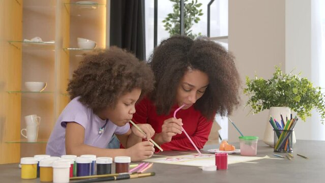 Cheerful charming curly African American mother and adorable happy elementary age daughter straw painting picture together, expressing inspiration and vivid imagination in artwork indoors.