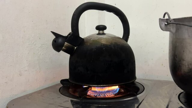 An old black burnt kettle stands on a gas stove