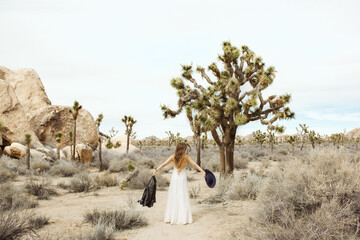 Woman in a boho style white dress and hat standing in the Joshua Tree desert
