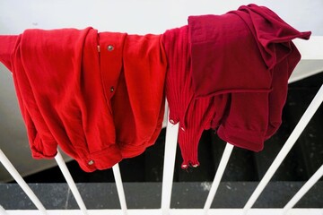Orangerote Bluse und rotes Trikot hängen über weißem Treppengeländer aus Stahl 