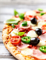 Pizza with ham, mozzarella cheese, cherry tomatoes, green and jalapeno pepper, black olives and fresh basil. Bright background. Close up	