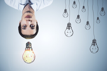 Upside down portrait of thoughtful businessman with drawn light bulbs on concrete wall background....