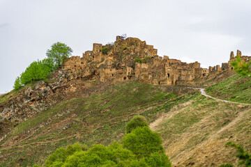 Ruins of ancient settlement in mountains. Ruined mountainous village Gamsutl in Dagestan republic. Old abandoned stone houses and buildings against spring landscape. Caucasian aul, Caucasus, Russia