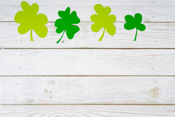 Green clover leaves cut from paper on a white wooden background. Greeting background with copyspace...