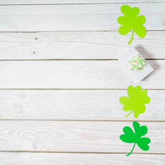Green shamrocks and giftbox with ribbon a white wooden table. Background for St. Patricks Day with...