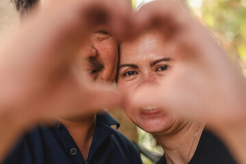 Loving Southeast Asian couple making heart shape with hands, celebrating 20 years of marriage