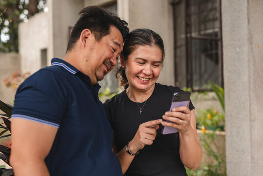 Southeast Asian couple enjoying social media on a phone outdoors - Powered by Adobe