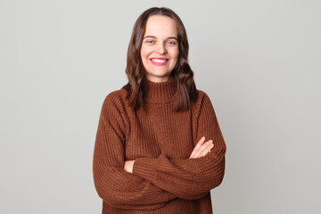 Confident satisfied Caucasian woman wearing brown sweater standing isolated over light gray...
