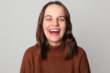 Laughing Caucasian woman wearing brown sweater standing isolated over light gray background being...