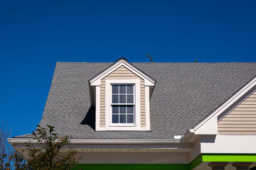 Gabled dormer window on the sloped shingle roof of a newly built family house in Boston, MA, USA