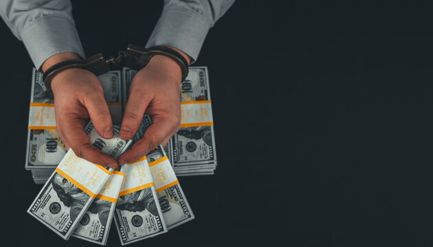 Top view of an official's hands in handcuffs and dollars on a black background. Copy space. A male official in handcuffs was caught taking a bribe. Concept of a corrupt official in handcuffs.