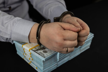 A corrupt official in handcuffs put his hands on stacks of dollars on a black background. Purchase...