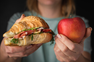 Woman hands holding freshly baked croissant with iberian ham, tomatoes and salad filling next to...