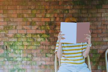 Close up teenage girl holding and reading book or magazine with vintage bick wall in reading room,...