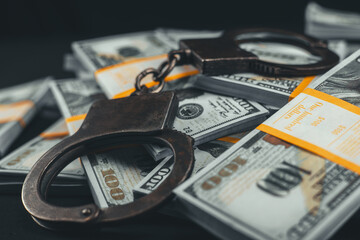 Close-up of handcuffs lying on top of dollars on a black background. Packs of dollars and handbrake boxes lie beautifully on a black background. Money fraud concept. - obrazy, fototapety, plakaty