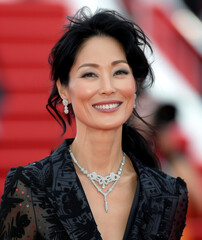 Photo of a 40-year-old woman with black hair in a low ponytail, smiling and looking at the camera on the red carpet in a suit with a silver diamond necklace