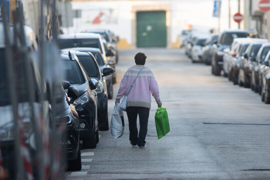An old woman walks down a street with a green bag